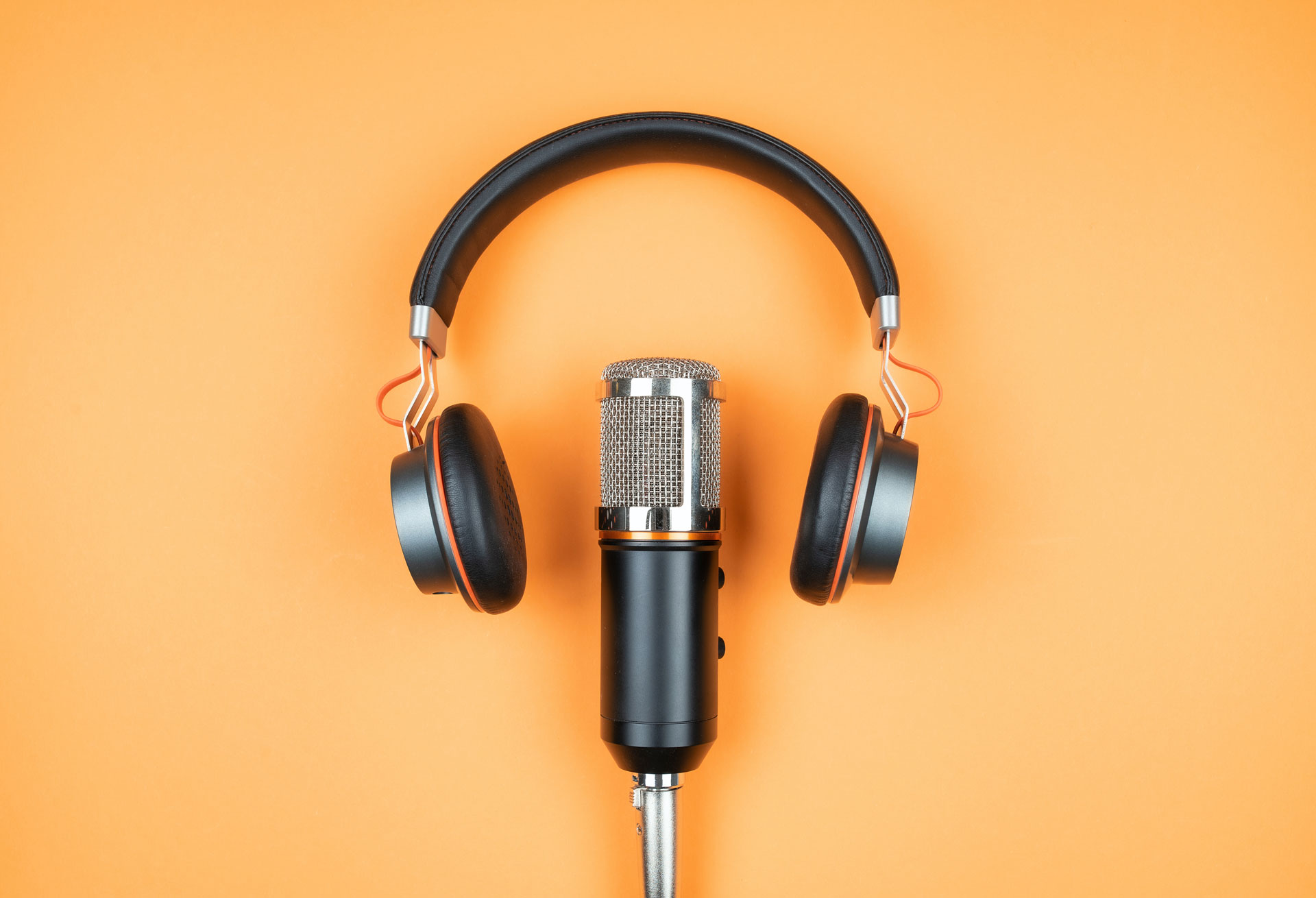 Podcast microphone and headphones on a light orange background.