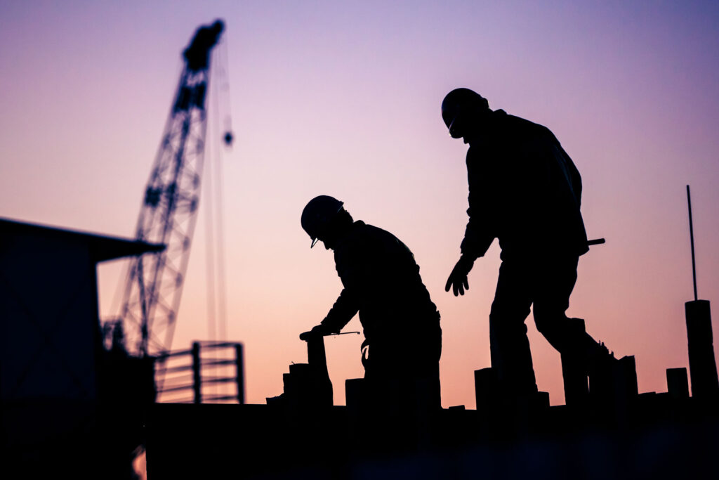 Silhouette of two construction workers in PPE against a dusky purple sky